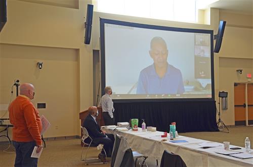 Mr Poore listening to virtual conference on large screen 